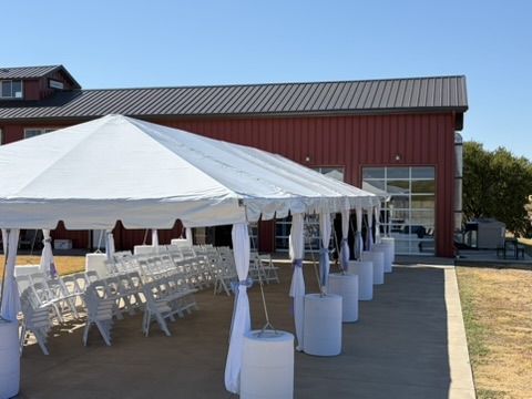 Outdoor tent with white chairs and draped poles beside the hangar