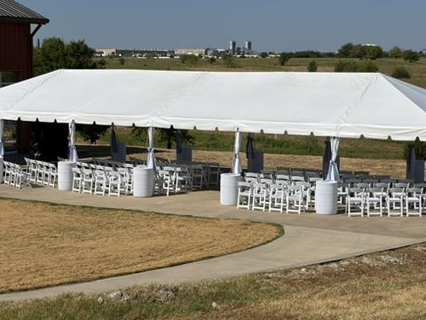 Rows of white chairs under the tent with fields beyond